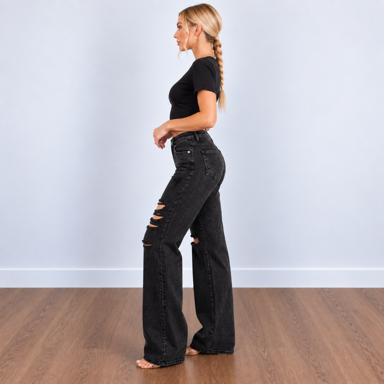 A woman stands in profile wearing black high-waisted wide-leg jeans with distressed rips at the knees.