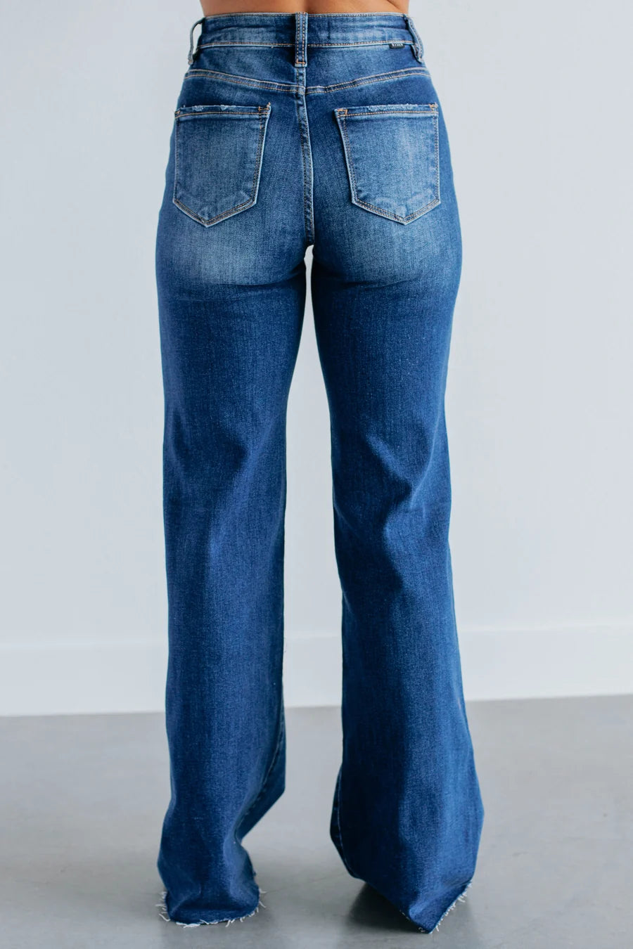 Rear view of a person wearing blue wide-leg jeans with a faded wash, standing against a light gray studio background.